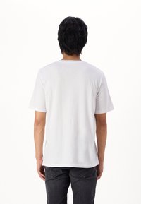 Witte katoenen t-shirt met een ronde hals, korte mouwen en een relaxte pasvorm, gecombineerd met donkergrijze jeans. Eenvoudig, strak ontwerp.