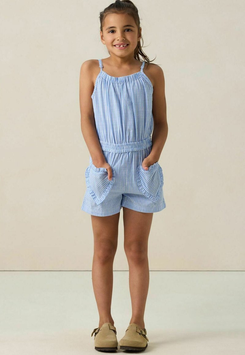 Rompers rayés bleus avec des fines bretelles, un décolleté froncé, une taille élastique et des poches en forme de cœur ; porté avec des chaussures marron clair.