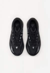 Chaussures de sport noires avec tige en mesh et synthétique, bout rond, design à lacets et détail à trois bandes sur le côté.