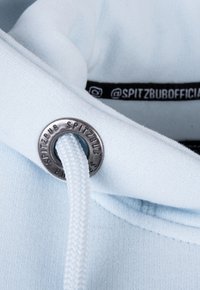 Hellblaues Kapuzenoberteil mit einer silbernen Öse und einem weißen geflochtenen Kordelzug. Verfügt über ein Markenetikett mit schwarzem Text am Ausschnitt. Weich im Griff.