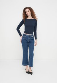 Μακρυμάνικη μπλούζα σε ναυτικό μπλε χρώμα συνδυασμένη με ψηλόμεσα, φαρδιά τζιν παντελόνια μπλε χρώματος. Τα τζιν έχουν εμπρόσθιες τσέπες και ελαφρά ξεθωριασμένα τελειώματα στα μπατζάκια.