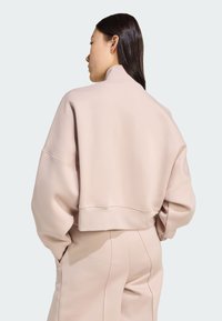 Sweatshirt cropped rosa chiaro con colletto alto e vestibilità ampia. Tessuto morbido, spalle cadute e dettagli di cuciture in vista. Accoppiato con pantaloni coordinati.