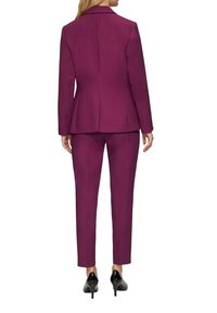 Lila skräddarsydd kostym med en figursydd jacka och smala byxor, tillverkad av ett smidigt tyg med rena linjer och minimal detaljering; matchad med svarta klackar.
