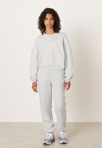 Svijetlosiva majica s dugim rukavima i odgovarajuće trenirka od mekog tkanja; karakterizirani su opuštenim krojem, rebrastim manžetnama i suptilnim logotipom.