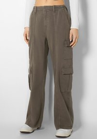Pantalones cargo en verde oliva, hechos de algodón, con un ajuste holgado, cintura elástica, múltiples bolsillos laterales y detalles de costura.