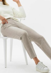 Pantalons beige ajustés avec une finition texturée, dotés de poches latérales. Associés à des baskets en cuir blanches et un haut en maille de couleur claire.