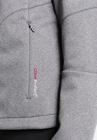 Gros plan sur la manche et le torse d'une veste en tissu gris avec une poche zippée verticale et « Clima Protect » brodé en rouge et blanc à l'avant.
