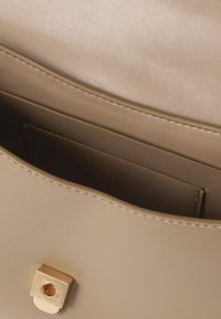 Κοντινό πλάνο από το εσωτερικό μπεζ δερμάτινης τσάντας, που δείχνει την ραμμένη τσέπη και τον χρυσό τετράγωνο κούμπωμα.