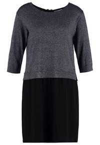 Haut en maille grise à manches trois-quarts porté sur une jupe ou une robe noire simple jusqu'aux genoux, présenté sur un fond blanc.