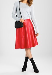 Falda A-line de cuero rojo, combinada con una blusa de manga larga azul claro y botas negras hasta el tobillo. Presenta una textura suave y un diseño sencillo.