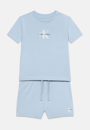 Lichtblauwe peuter set met korte mouwen shirt en korte broek, beide met Calvin Klein-logo's aan de voorkant en schouderdrukknopen op het shirt.