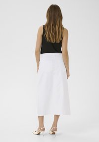 Fustă maxi din denim alb, cu buzunare la spate, asortată cu un top negru fără mâneci și sandale cu toc nude, văzută din spate.