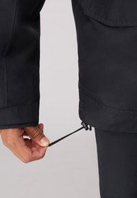 Schwarze wasserdichte Jacke mit einem Kordelzug am Saum; die Textur ist glatt, verfügt über einen verstellbaren Stopper und hat eine leicht lockere Passform.