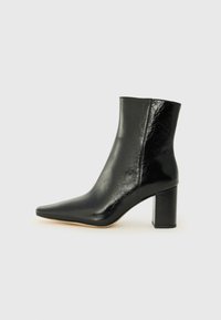 Stivale alla caviglia nero in pelle lucida con punta affusolata e tacco squadrato e corposo. Presenta una texture liscia e un design minimalista.