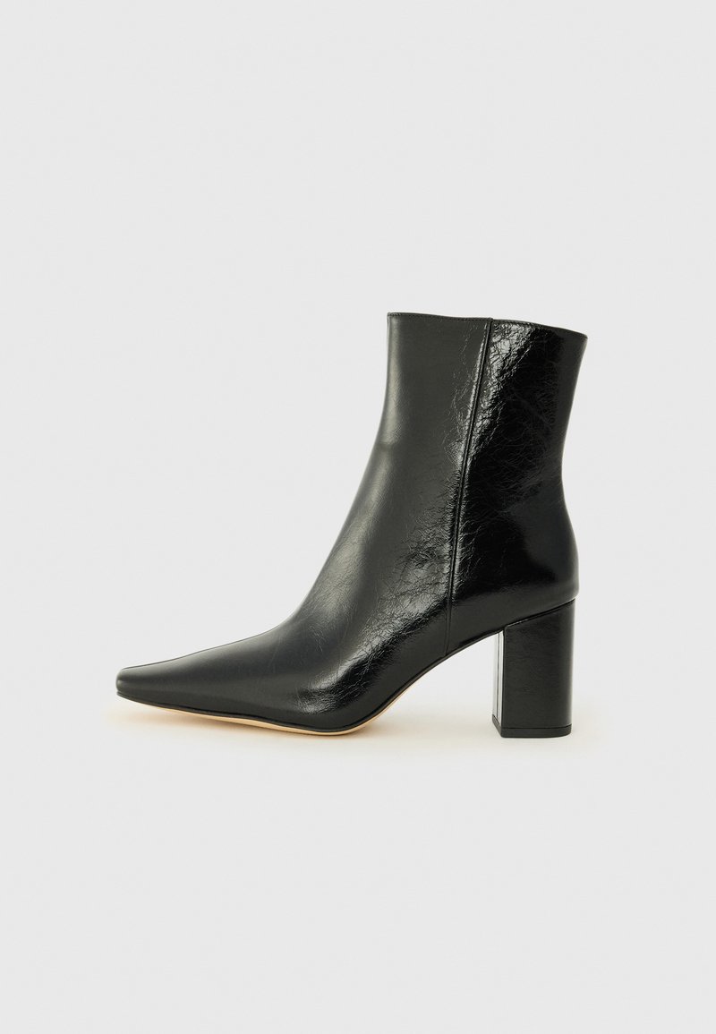 Stivale alla caviglia nero in pelle lucida con punta affusolata e tacco squadrato e corposo. Presenta una texture liscia e un design minimalista.