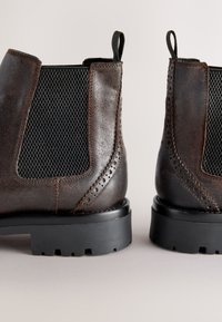 Braune Leder-Knöchelstiefel mit einer strukturierten schwarzen elastischen Einsätzen, geschwungenem Design, Zuglaschen und einer robusten Gummisohle mit Profil.