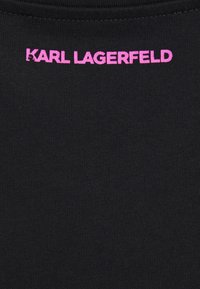 Svart tyg med en slät textur som har en rosa "KARL LAGERFELD"-logotyp högst upp. Enkel design, inga ytterligare mönster eller accenter.