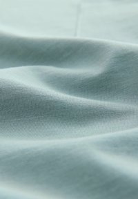 Lichtblauwe stof met een gladde textuur, voorzien van subtiele ribbels en zachte plooien, die een zachte, vloeiende uitstraling creëren.