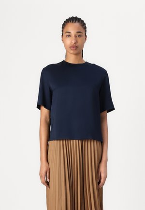 Mørkeblå kortermet topp med rund hals. Glatt tekstur, avslappet passform og rett søm, brukt med en plissert beige skjørt.