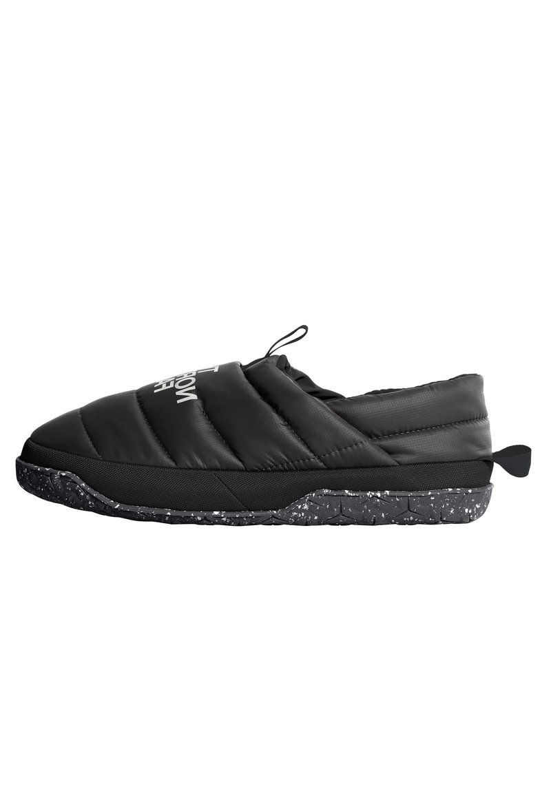 Musta pehmustettu liukuva kenkä, jossa on teksturoitu päällinen, speckled-mustalla pohjalla ja takana vetotappi. Logo-yksityiskohta päällisessä.