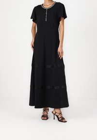 Musta maxi-mekko lyhyillä hihoilla, jossa on koristeellinen vetskari ja vaakasuorat mustat raidat alaosassa, sileä rakenne.