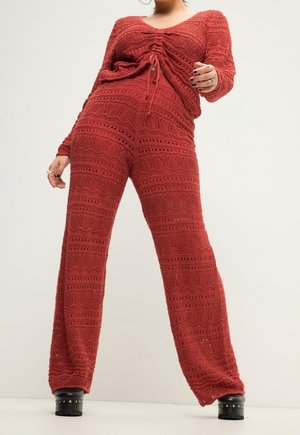Personne portant un pull en tricot rouge à motifs et un pantalon large assorti, associés à des chaussures plateformes noires cloutées.