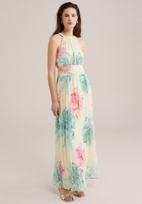 Robe maxi en tissu léger, ornée d'un motif floral rose et teal sur un fond jaune clair. Design fluide avec une taille cintrée.