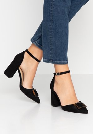 Sorte ruskindsstiletter med spids tå, ankelrem og en stor spænde i skildpadde-mønster foran.