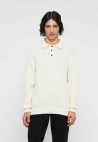 Cremfarbener gestrickter Poloshirt mit Kragen, drei dunklen Knöpfen, gerippten Bündchen und lässigem Schnitt.