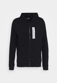Hodie zippé noir en tissu doux, avec un patch logo sur le devant, deux poches latérales, des poignets côtelés et une capuche à cordon.