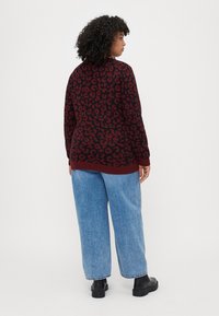 Suéter com padrão de leopardo em tons de bordeaux, com um decote redondo, combinado com jeans de perna larga em azul claro. Tecido texturizado e punhos canelados. Botas de tornozelo pretas.