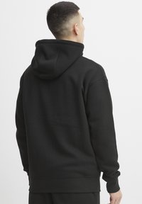 Haut à capuche noir en mélange de coton, avec une coupe décontractée, un capuchon à cordon de serrage et des poignets côtelés. Texture lisse avec des détails de marque minimalistes.