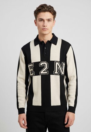 Junger Mann trägt ein schwarz-weißes langärmeliges Poloshirt mit vertikalen Streifen und "E 2 N" Buchstaben über der Brust.