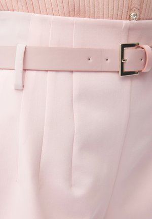 Pantaloni rosa chiaro con pieghe e una cintura rosa abbinata con fibbia rettangolare argento indossati con un maglione rosa a coste.