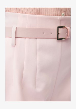 Lichtroze broek met plooien en een bijpassende roze riem met een zilverkleurige rechthoekige gesp, gedragen met een geribbelde roze trui.