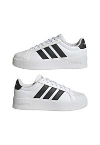 Witte leren sneakers met zwarte drie strepen en hielaccenten, voorzien van een dikke witte zool en een ronde neusvorm.