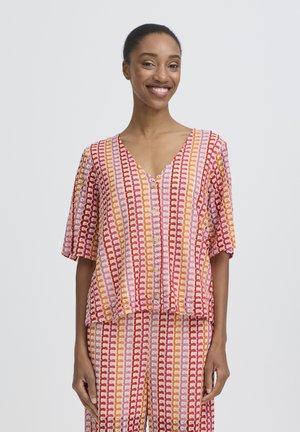 Femme souriante, portant un ensemble assorti en tricot composé d'un haut à manches courtes et d'un pantalon avec un motif à rayures verticales en rouge, orange, rose et crème.