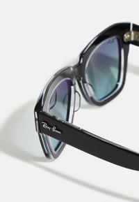 Ochelarii de soare Ray-Ban negri au un cadru supradimensionat, unghiular, cu lentile gradient. Brațele au o finisare lucioasă și detalii cu logo în stil cursiv.