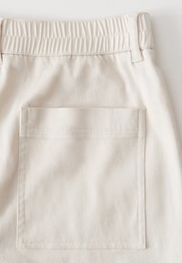 Shorts en tissu beige clair avec une large taille élastique et une grande poche arrière, présentant une texture lisse et des détails de couture soignés.
