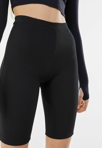 Black bike shorts made from stretchy, textured fabric. They feature a high waistband and a mid-thigh length with a smooth, fitted design.