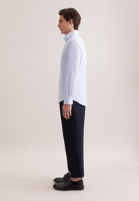 Camicia a righe blu e bianche con bottoni, abbinata a pantaloni blu navy e scarpe nere. La camicia presenta un colletto classico e polsini standard.