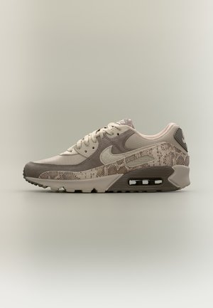 Vue de profil d’une sneaker Nike Air Max beige et grise, avec des empiècements à motifs, un logo Swoosh et un amorti Air visible.