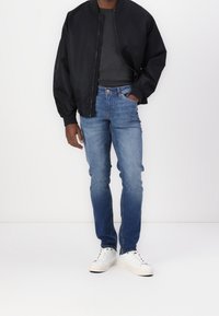 Černá bomber bunda, šedé tričko, modré džíny, bílé tenisky. Neformální outfit s jednobarevným designem a uvolněným střihem.