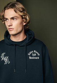 Sudadera azul marino de mezcla de algodón, con letras blancas que dicen "LA" y "Abbot Kinney 349 Boulevard", con capucha ajustable y tejido texturizado.