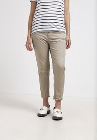 Béžové kalhoty slim fit, s knoflíkovým a zipovým zapínáním, s manžetami a hladkým materiálem. V kombinaci s proužkovanou košilí a bílými dřeváky.