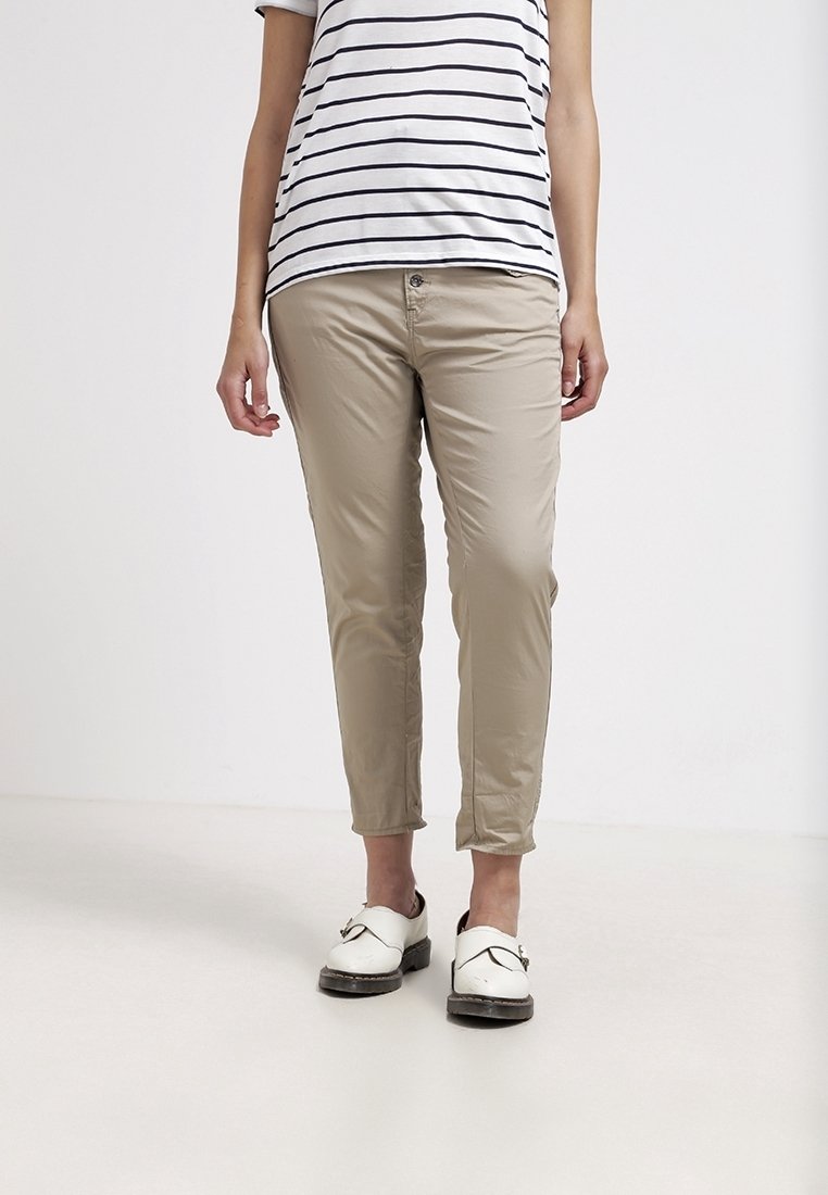 Béžové kalhoty slim fit, s knoflíkovým a zipovým zapínáním, s manžetami a hladkým materiálem. V kombinaci s proužkovanou košilí a bílými dřeváky.