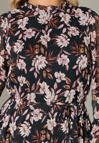 Svart blommig klänning med rosa och bruna blommor, genomskinliga långa ärmar, en volangkrage och en knytning i midjan med en lätt textur.