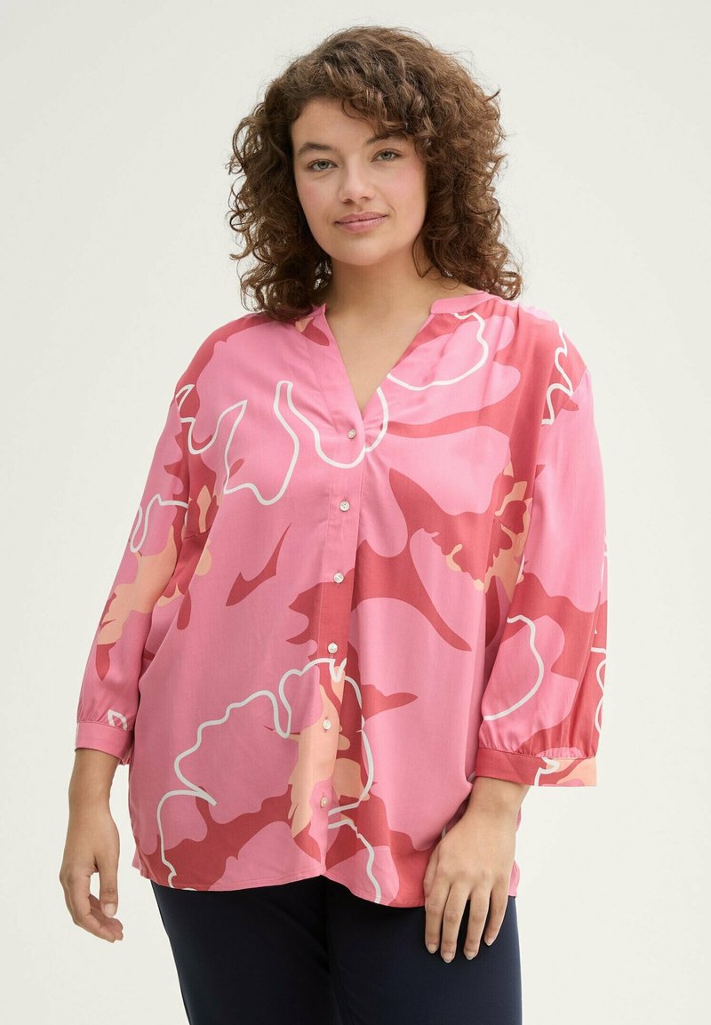 Blouse florale rose avec un décolleté en V, des manches longues et une fermeture à boutons. Conçue avec des motifs abstraits dans des nuances de rose et de blanc.