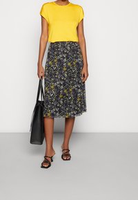 Top giallo a maniche corte e gonna midi con stampa floreale in tonalità scure. Accompagnata da sandali neri con tacco a blocco e una borsa a tracolla.