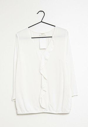 White long-sleeve blouse with a V-neck and ruffled front. Made of smooth fabric, features a rounded hem and a hanging tag.